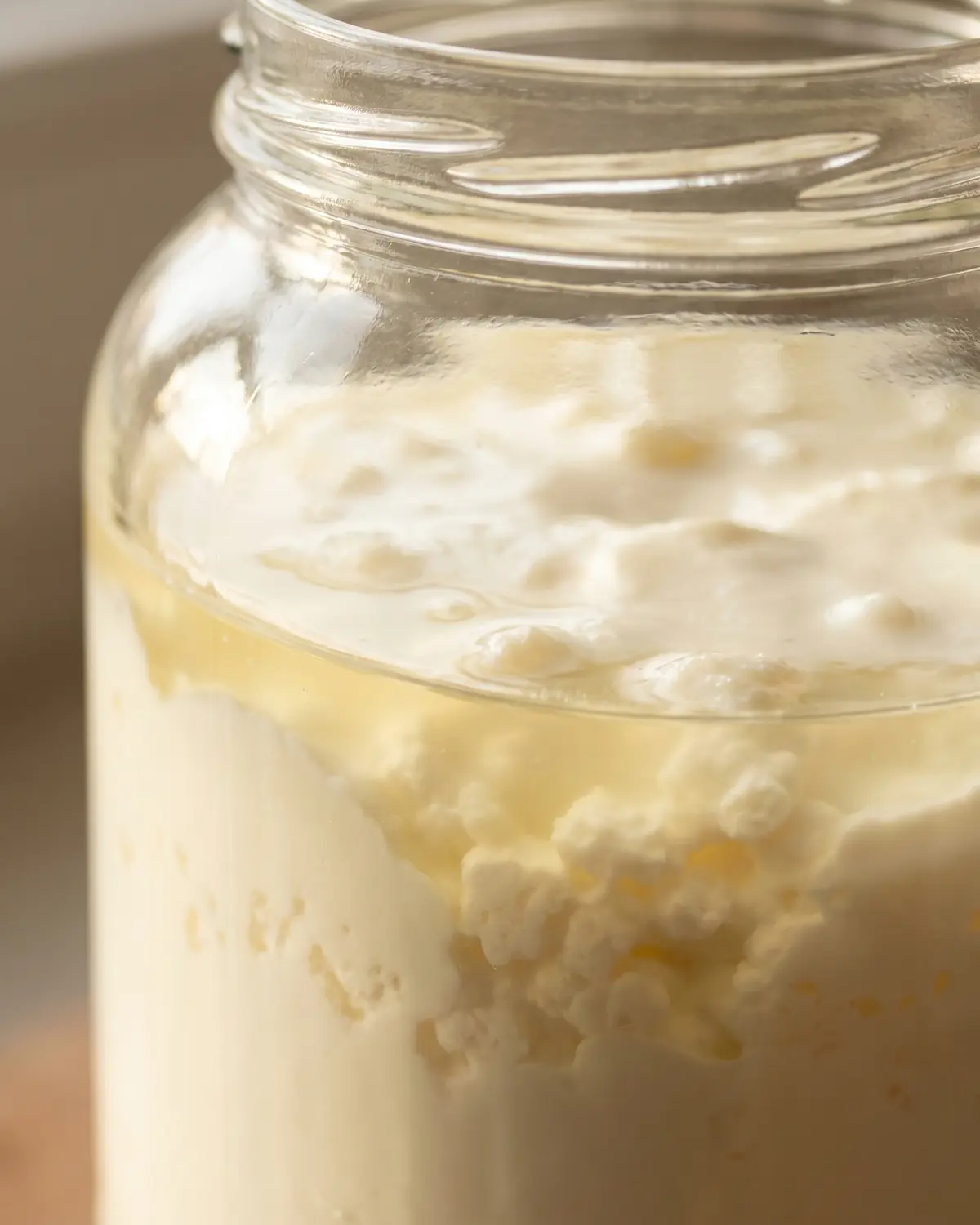 kéfir como se toma Tarro de kéfir de leche con separación visible entre suero y crema durante la fermentación.