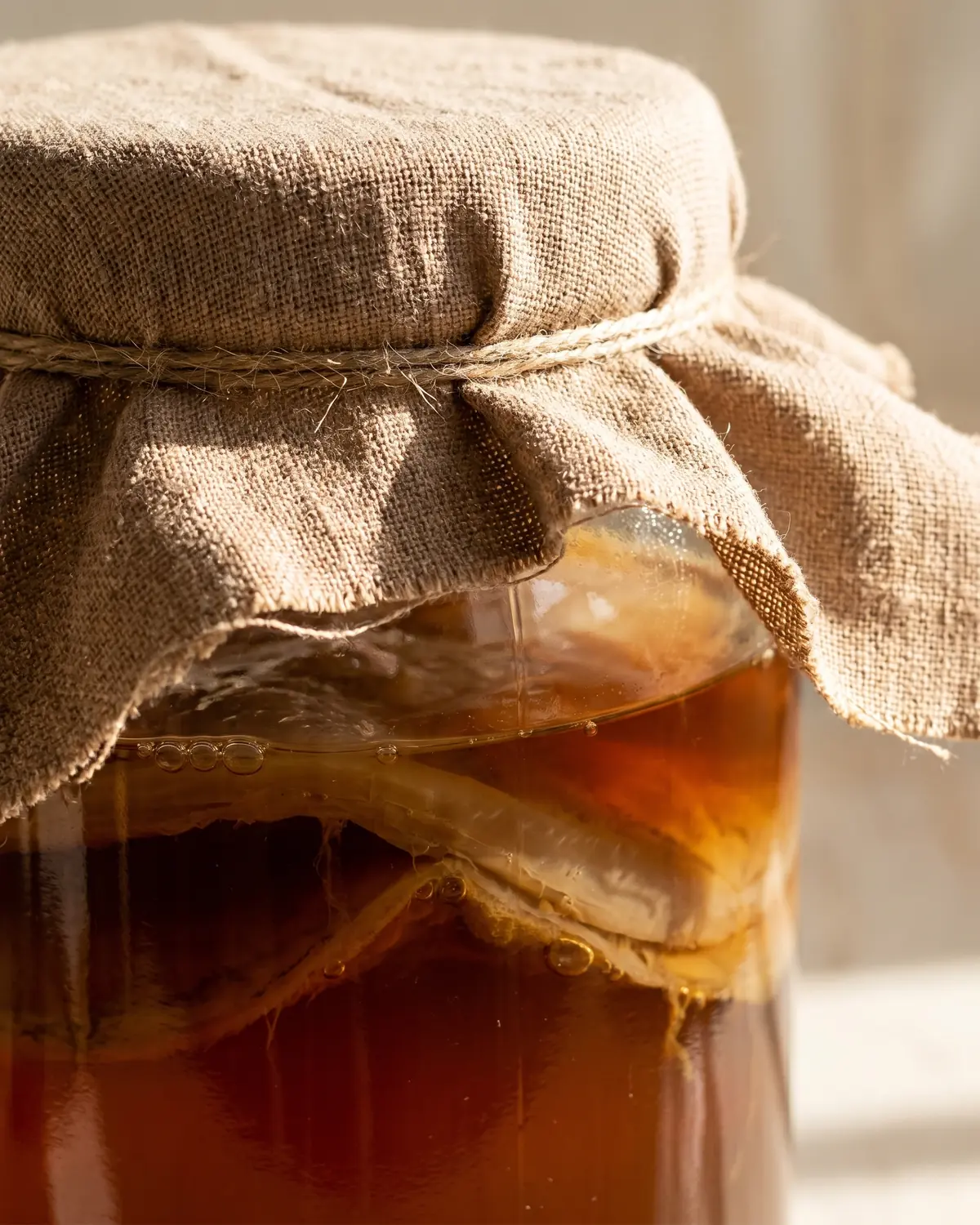 Primer plano de un tarro de kombucha cubierto con pa&ntilde;o de algod&oacute;n y t&eacute; oscuro bajo la tela.