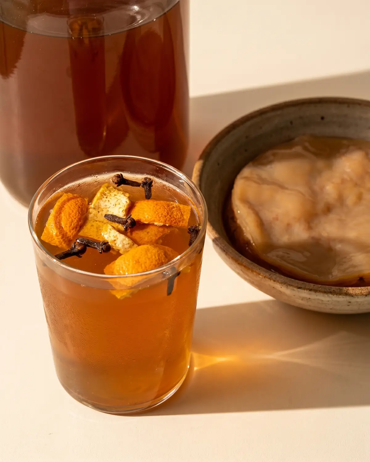 kombucha opiniones Vaso de kombucha ámbar con piel de naranja seca y clavo bajo una sombra suave de tarde.