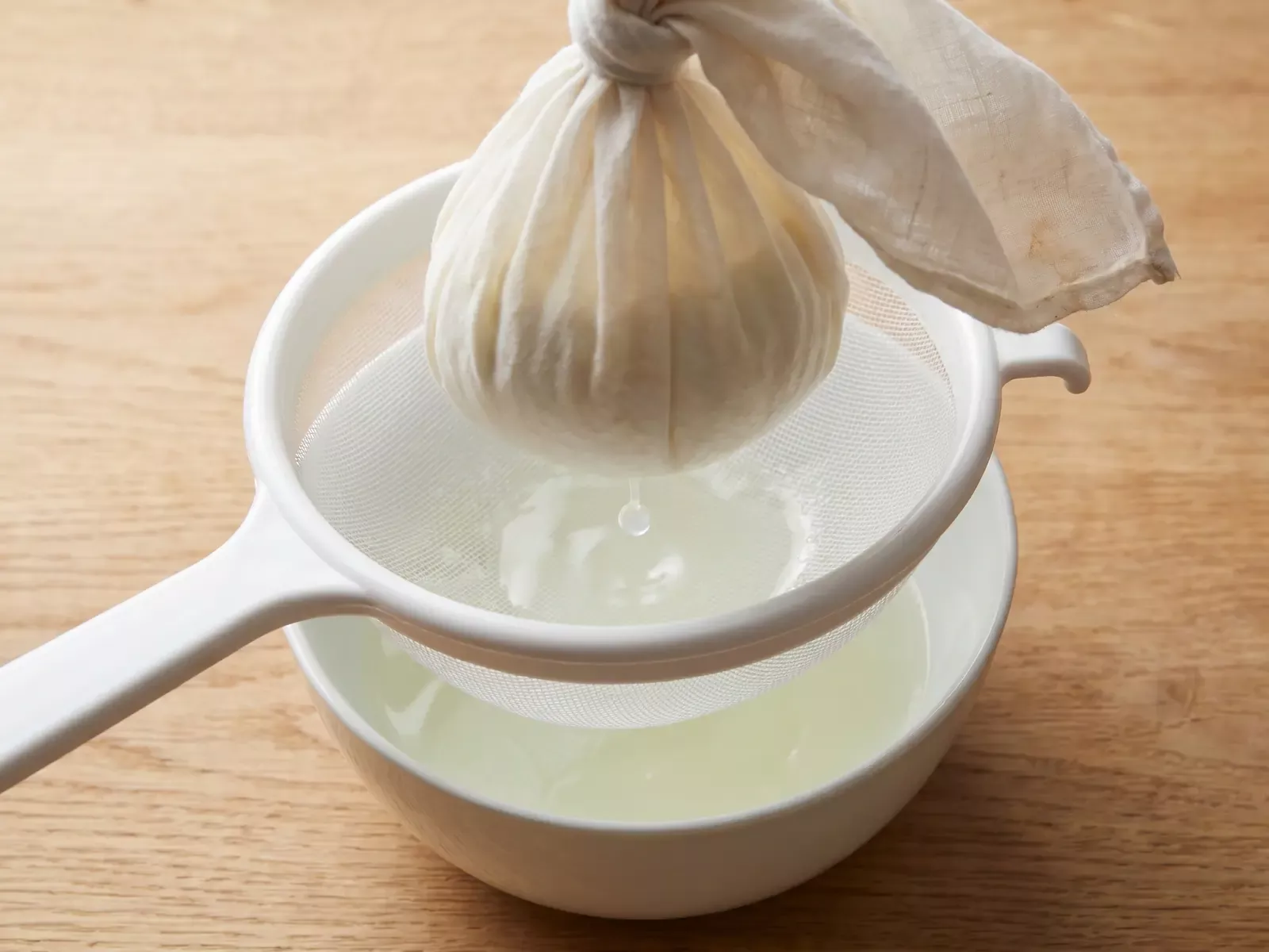 Yogur casero escurri&eacute;ndose en un colador con tela mientras cae una gota de suero.